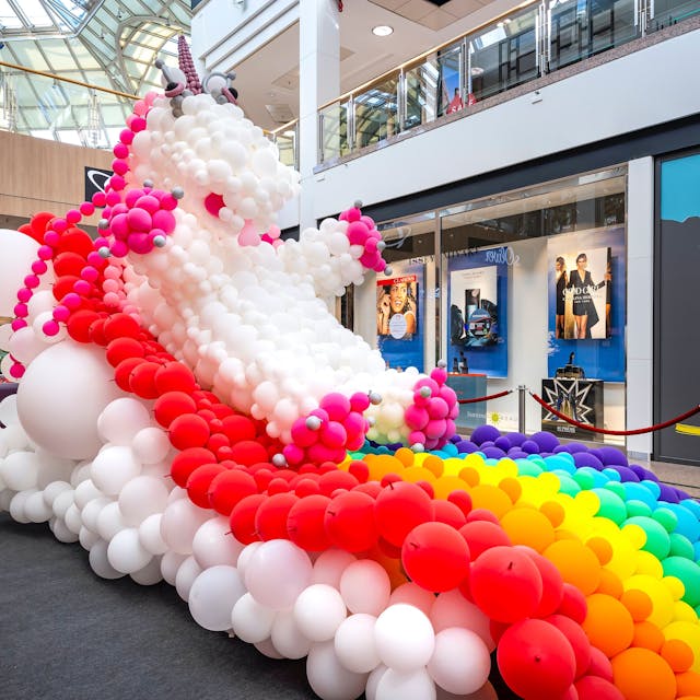 Ein Einhorn mit Regenbogen aus Luftballons steht im Erdgeschoss eiens großen Einkaufszentrums.