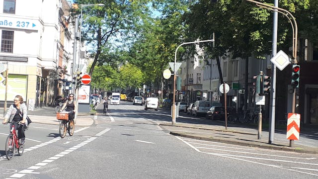 Die Kreuzung Neusser/Kempener/ Auerstraße ist zu sehen. Drei Straßen treffen aufeinander, Radfahrerinnen radeln über die Kreuzung.&nbsp;