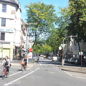 Die Kreuzung Neusser/Kempener/ Auerstraße ist zu sehen. Drei Straßen treffen aufeinander, Radfahrerinnen radeln über die Kreuzung.&nbsp;