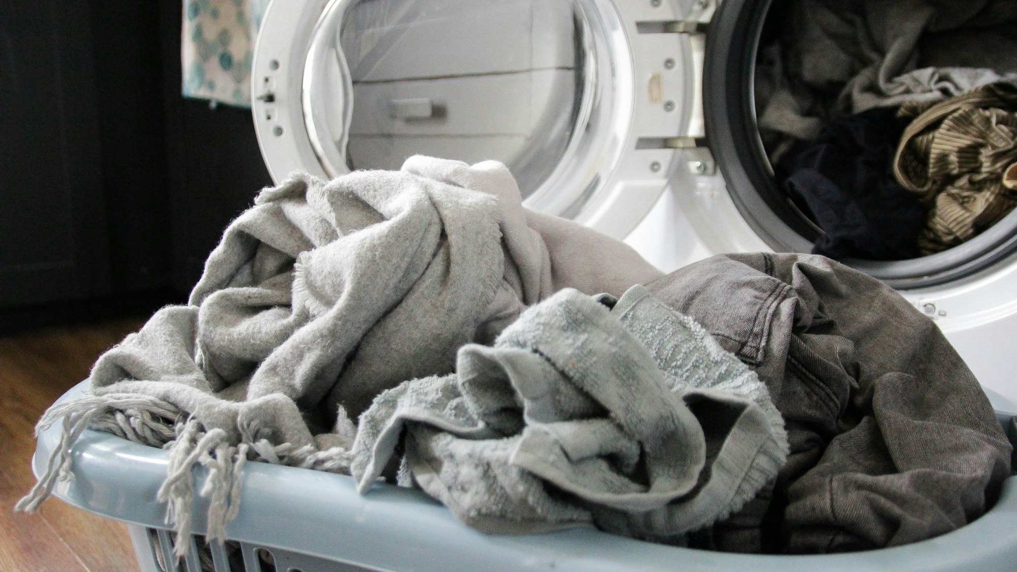 Auf dem Foto sieht man einen Wäschekorb voll mit Wäsche vor einer offenen Waschmaschine.