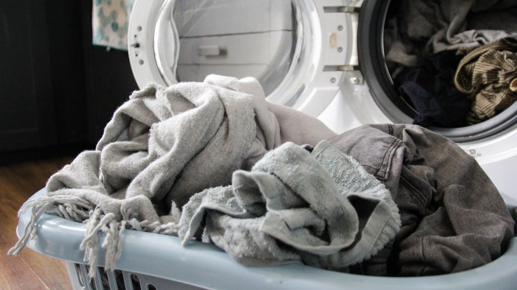 Auf dem Foto sieht man einen Wäschekorb voll mit Wäsche vor einer offenen Waschmaschine.&nbsp;