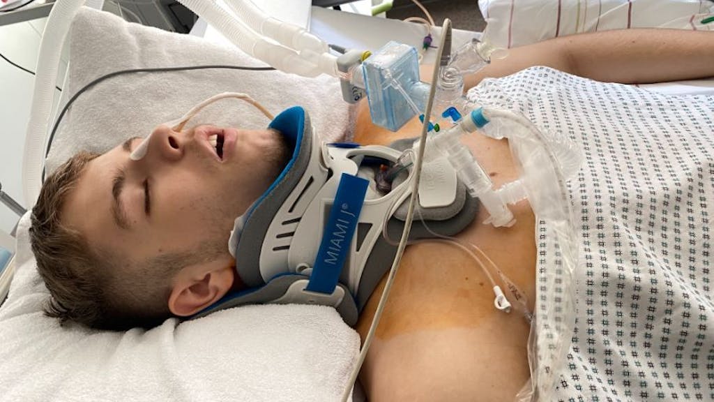 Junger Mann liegt mit Halskrause und an Geräte angeschlossen in einem Krankenbett.