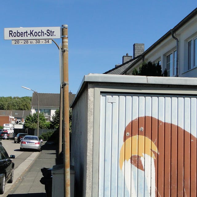 Ein Straßenschild mit der Aufschrift „Robert-Koch-Str.“ steht an einer Straßenecke.