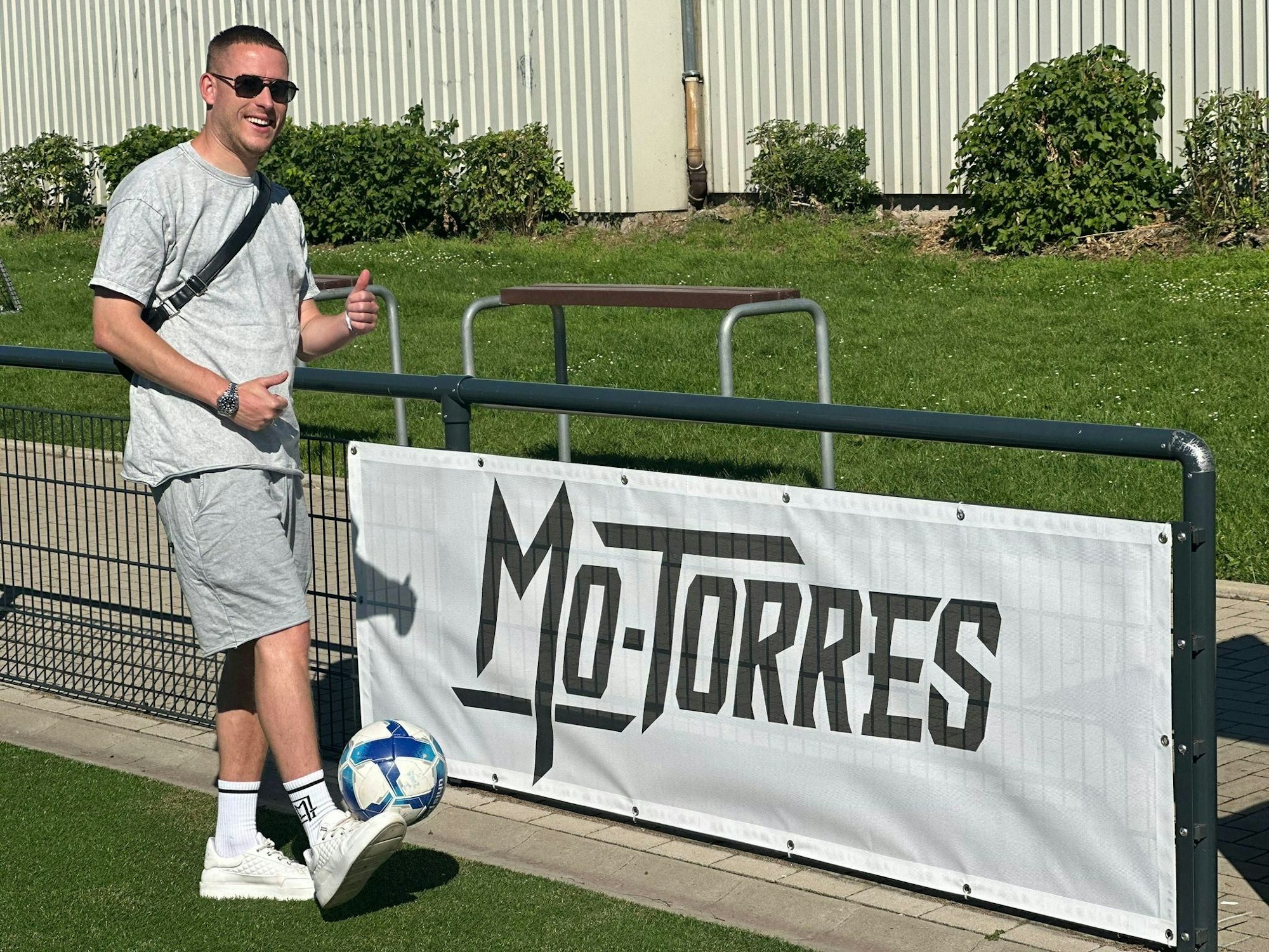 Mo-Torres steht vor seinem Banner auf dem Fußballplatz von DJK Roland West.