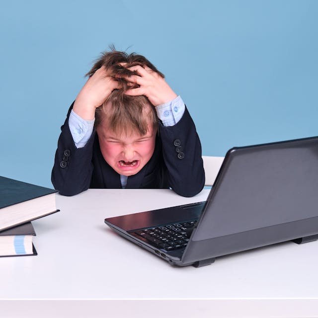 Ein kleiner Junge mit dunkelblauem Anzug sitzt wütend vor dem Computer.
