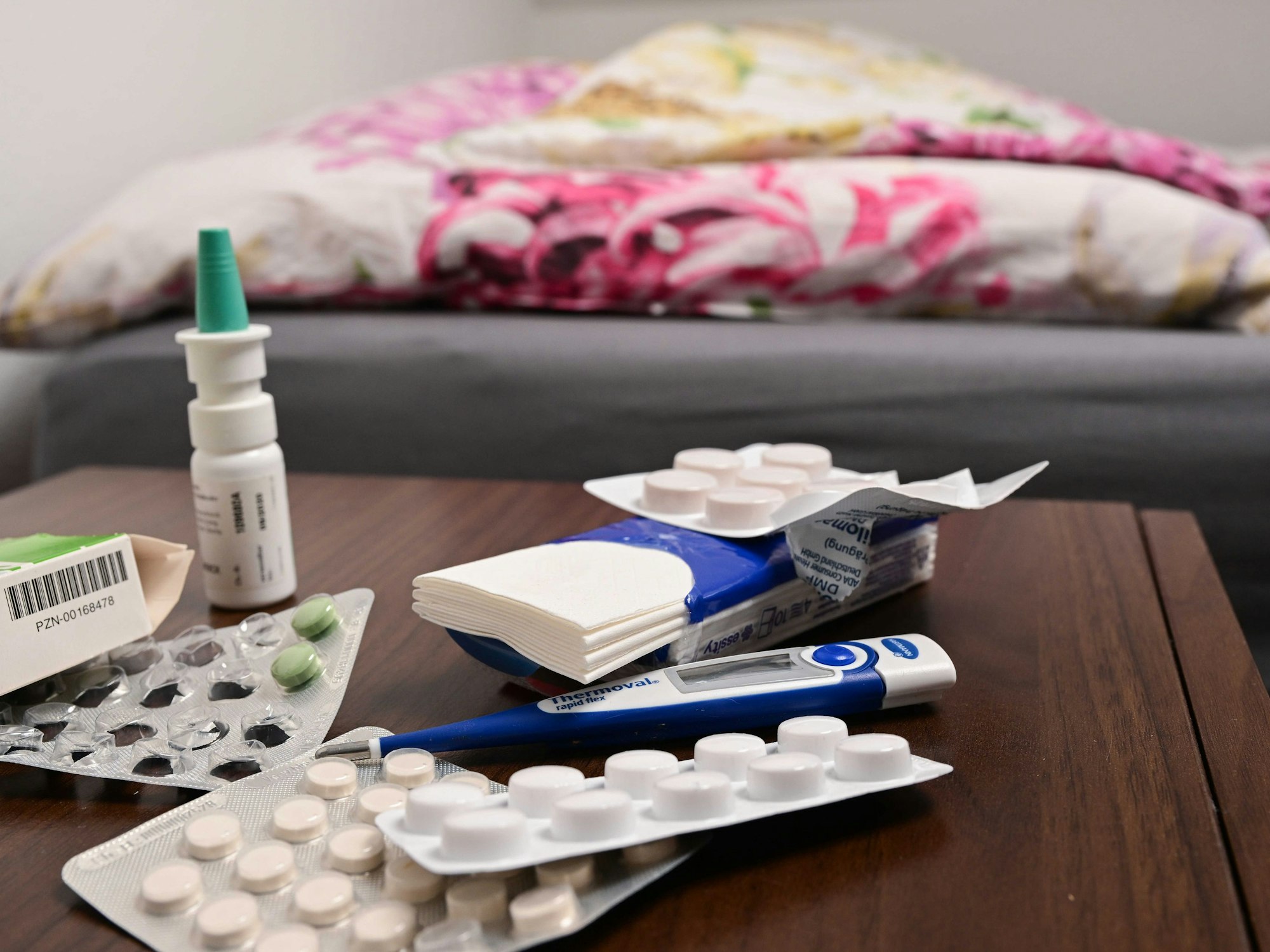 Ein Fieberthermometer und Medikamente liegen auf einem Nachttisch (gestellte Szene).