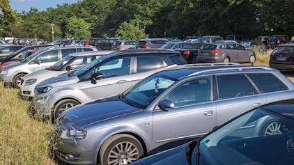 Viele Autos auf einem Parkplatz zwischen Büschen und Bäumen.