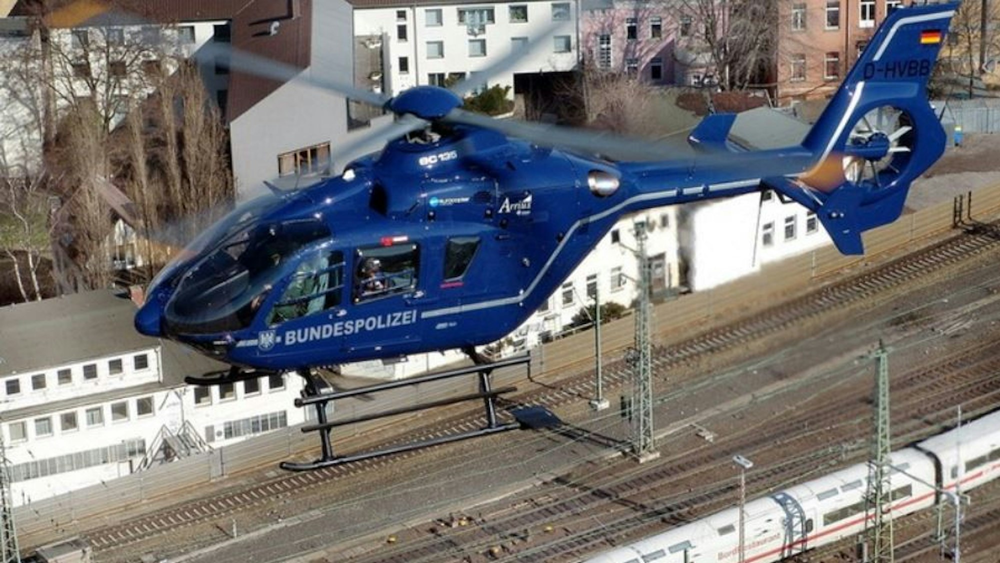 Blauer Hubschrauber der Bundespolizei kreist in der Luft, unten sind Bahngleise zu sehen.