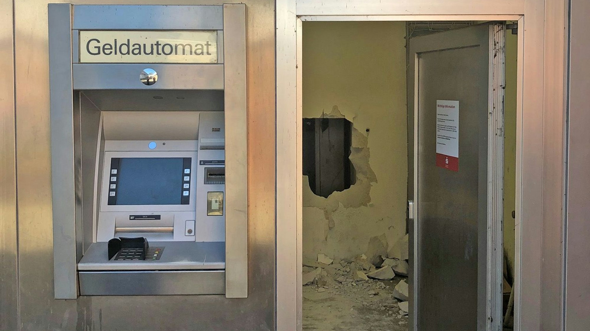 Geldautomat in einer Ladenfiliale, im Hintergrund sieht man eine durchbrochene Wand.