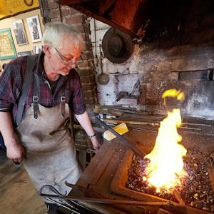 Der Schmied Stefan Pütz steht in einer alten Werkstatt an einem Kohlenfeuer.&nbsp;