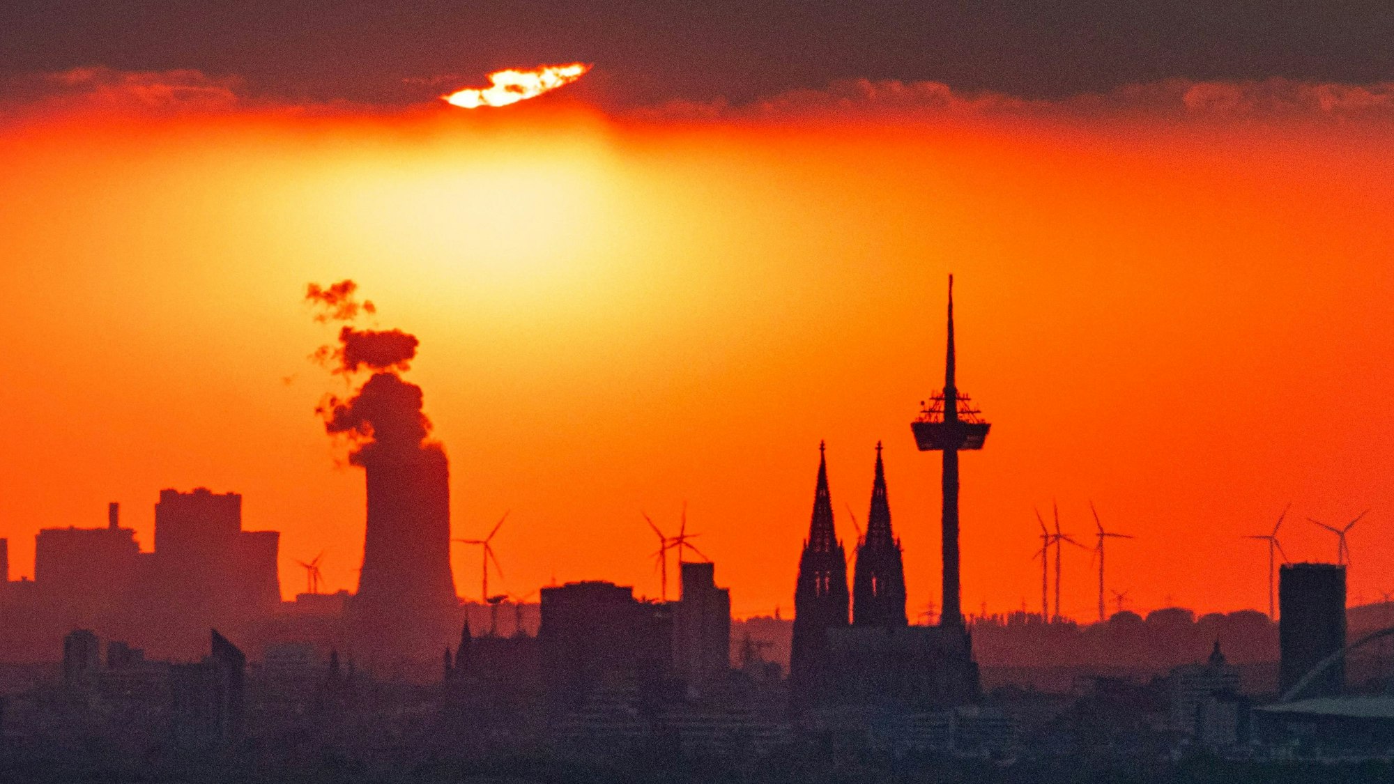 Die Sonne steht am Abend kurz vor Sonneuntergang hinter Wolken über der Stadt. (Symbolbild)