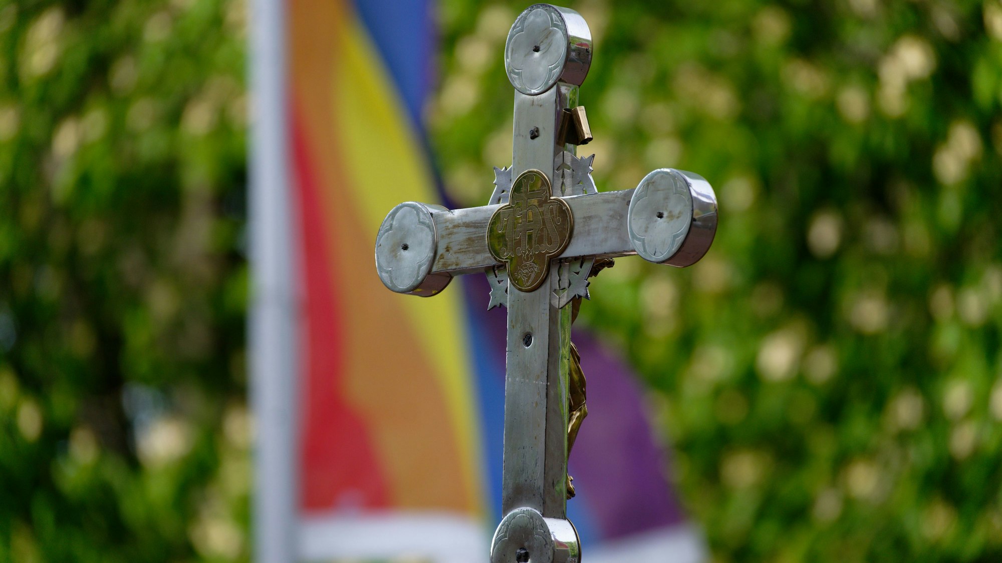 Ein Kreuz vor einer Regenbogenfahne.