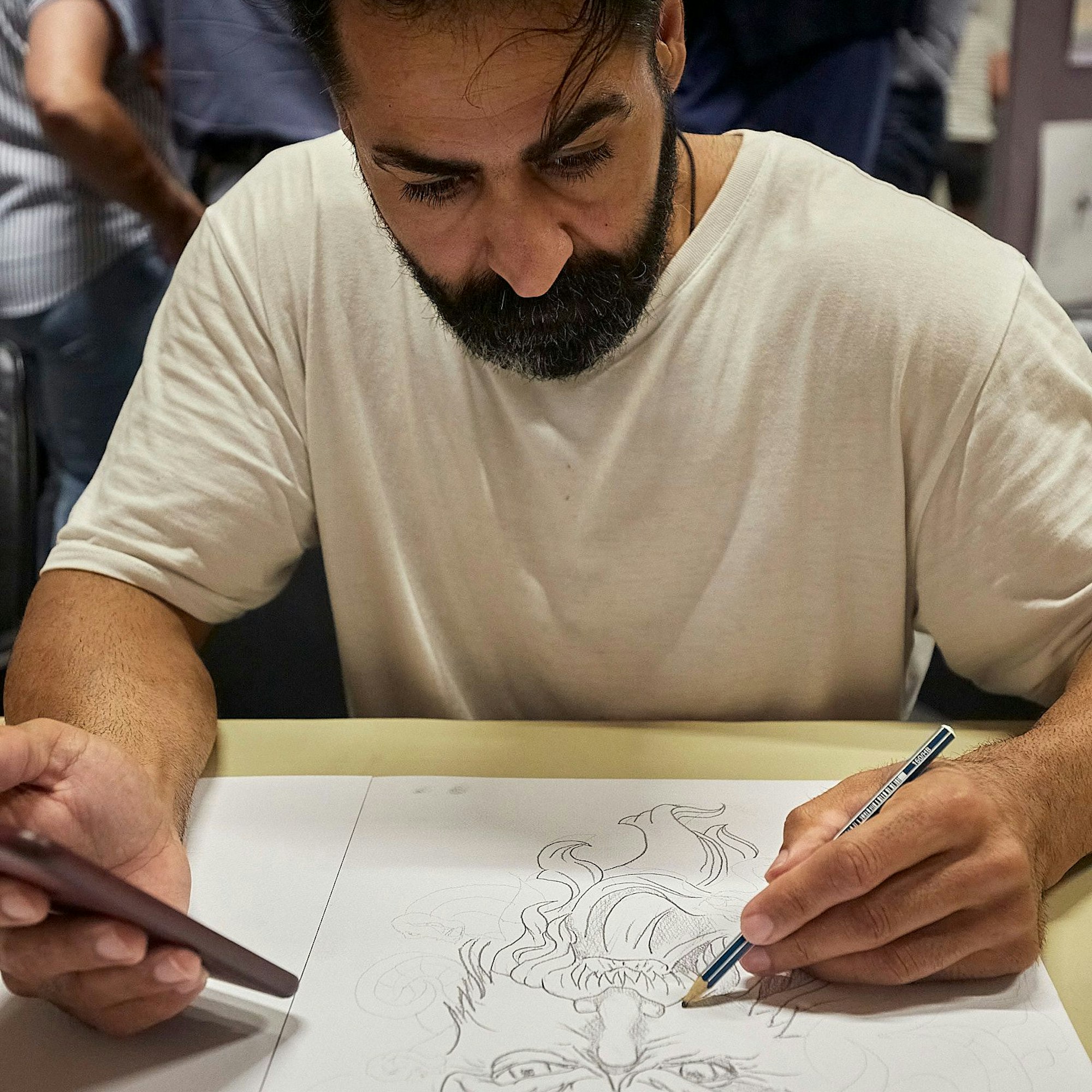 Der Iraner Obadi zeichnet mit einem Bleistift ein Bild. In der anderen Hand hält er ein Smartphone.