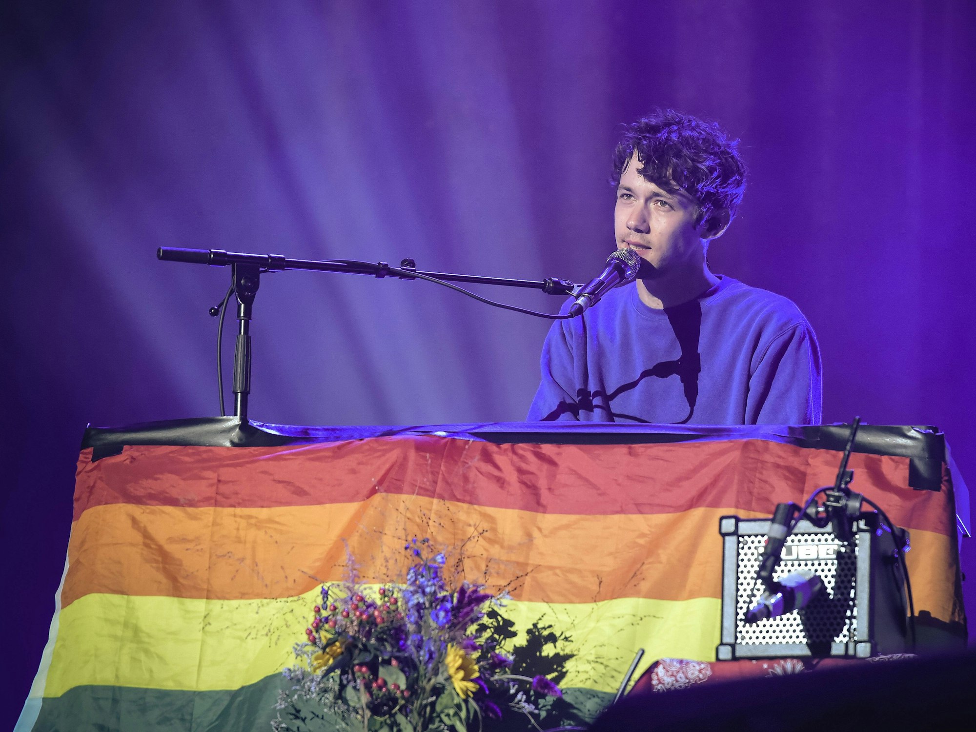 Henning May sitzt an im September 2022 beim Lollapalooza Festival in Berlin am Klavier. Dieses ist mit einer riesigen Regenbogenflagge geschmückt.
