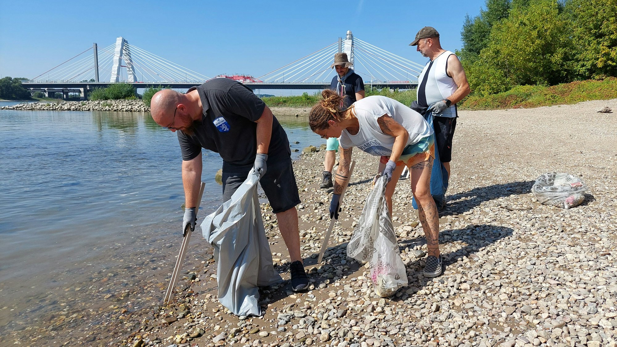 Menschen sammeln am Rheinufer Müll.