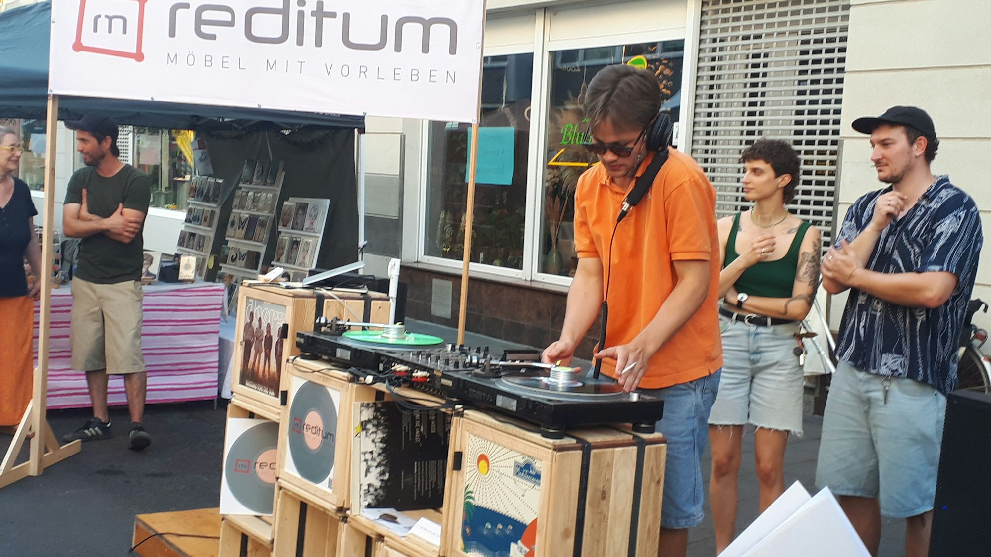 Ein junger Mann steht hinter einem DJ-Pult auf Holzkisten am Straßenrand.