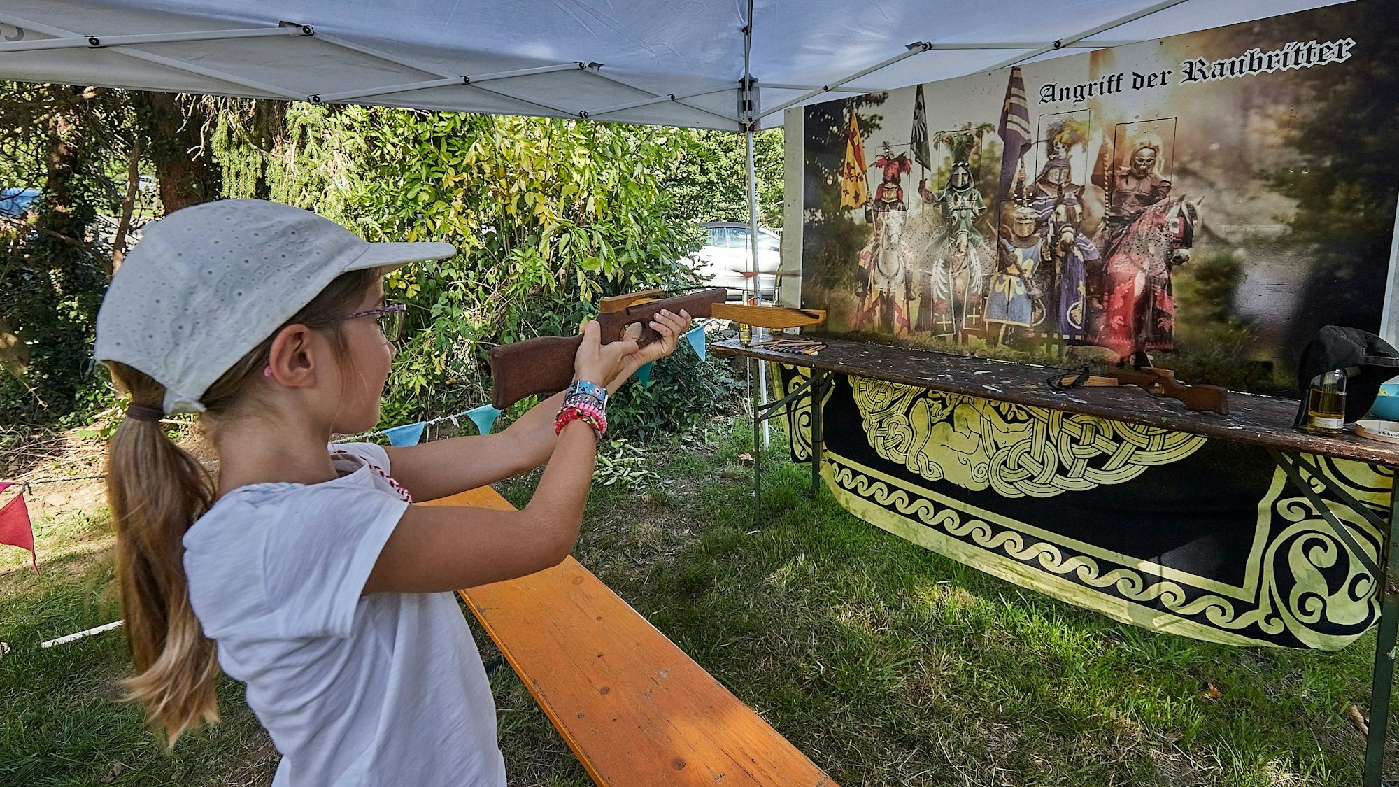 Ein Mädchen zielt bei einem Mittelalterfest mit einer Kinder-Armbrust auf ein Ziel.