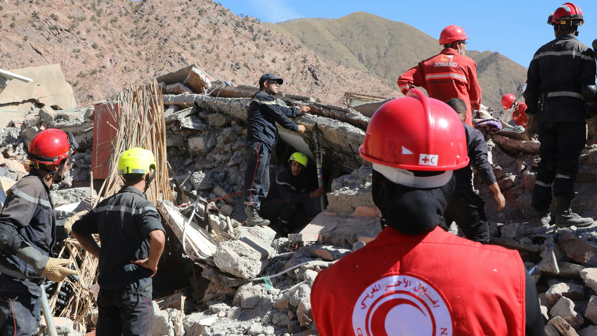 In dem Bild stehen mehrere Rettungskräfte vor Trümmern in Talat N'Yaaqoub (Marokko) und suchen nach Überlebenden.