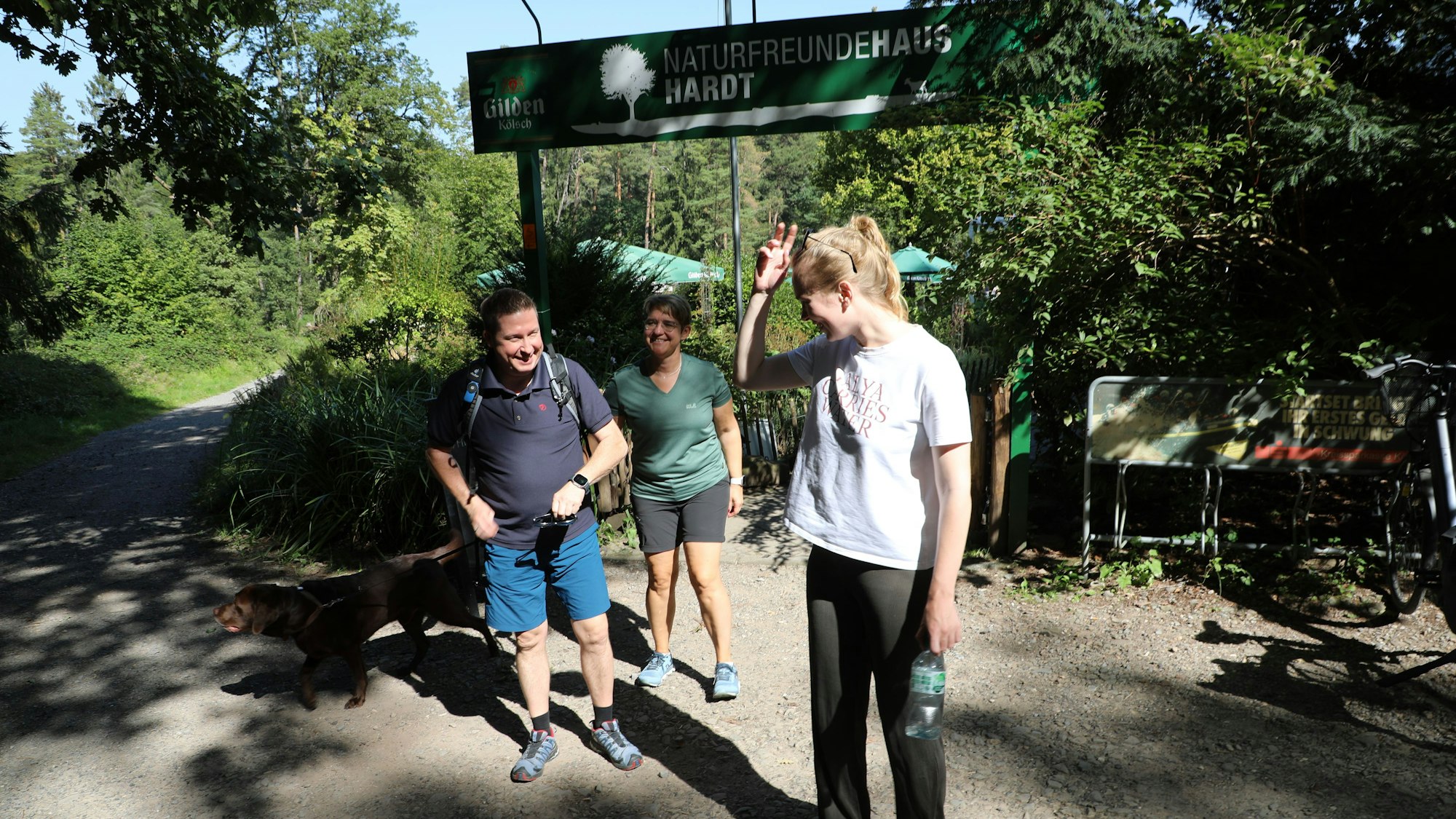 Drei Menschen vor einem Gastronomie-Schild mit der Aufschrift „Naturfreundehaus Hardt.“