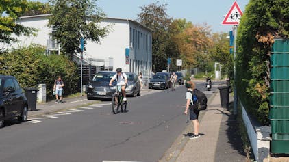 Das Foto zeigt Radfahrer vor einer Schule und Kinder auf ihrem Heimweg.