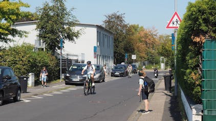 Das Foto zeigt Radfahrer vor einer Schule und Kinder auf ihrem Heimweg.