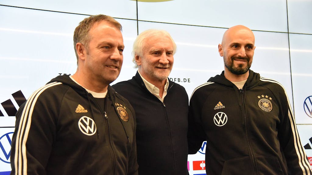 Hansi Flick, Rudi Völler und Antonio Di Salvo stehen bei einer Pressekonferenz nebeneinander.