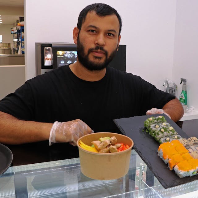 Das Bild zeigt einen Mann, der in seinem Restaurant Sushi und Bowls anbietet.