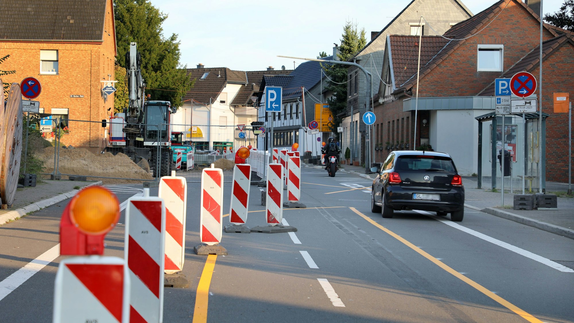 Ein Auto und ein Motorrad fahren durch eine verengte Straße an einer Baustelle in Overath-Heiligenhaus.