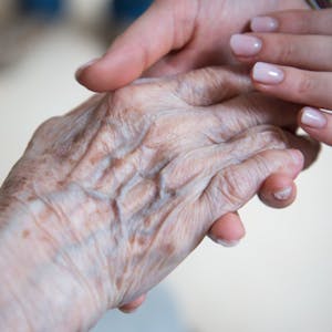 Eine Pflegerin hält die Hand einer Seniorin.