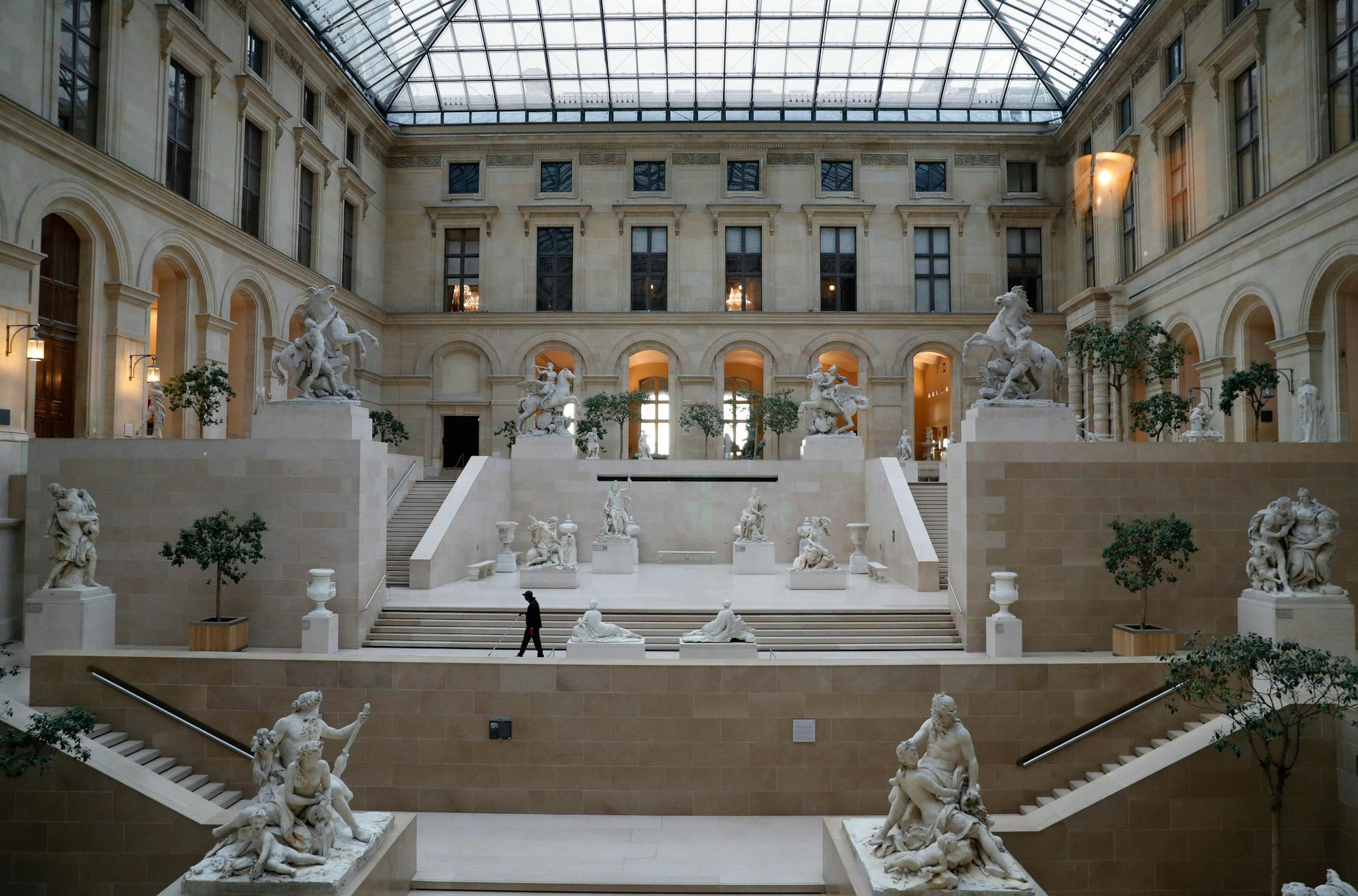 Eine Halle des Musée du Louvre. Neben den Treppen stehen zahlreiche Skulpturen.