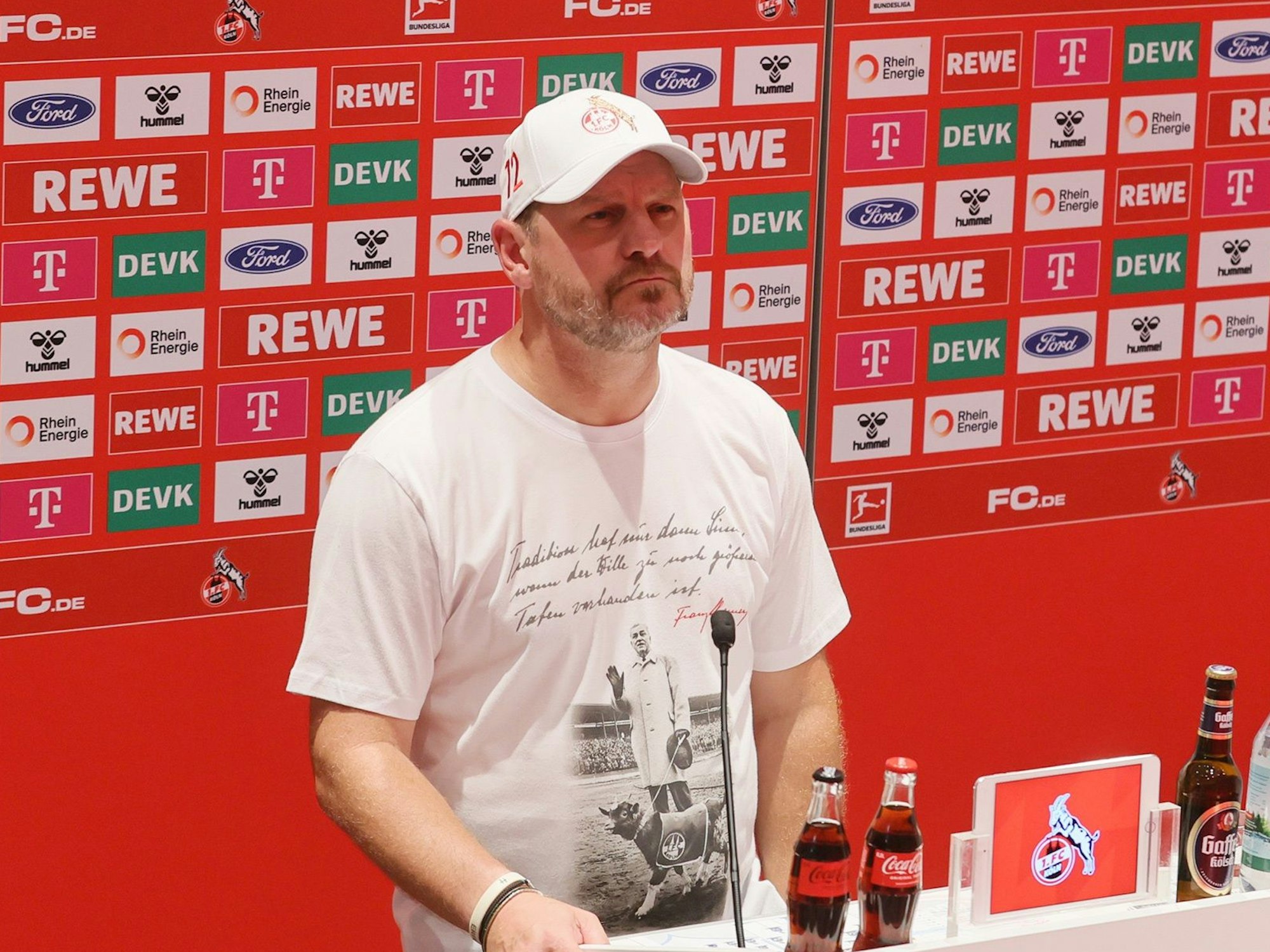 Steffen Baumgart steht vor einer Werbetafel des 1. FC Köln.