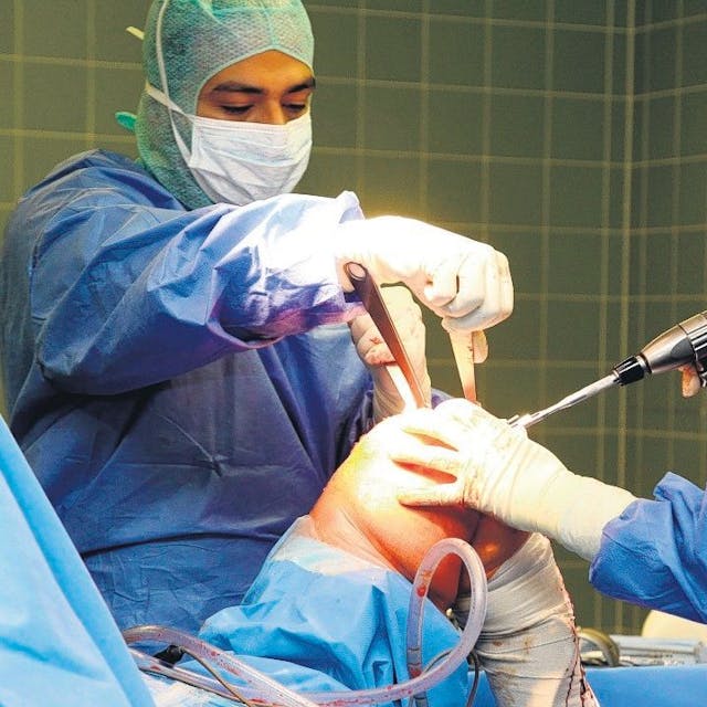 Zwei Ärzte in OP-Kleidung, Masken und Hauben arbeiten an einem Knie.&nbsp;