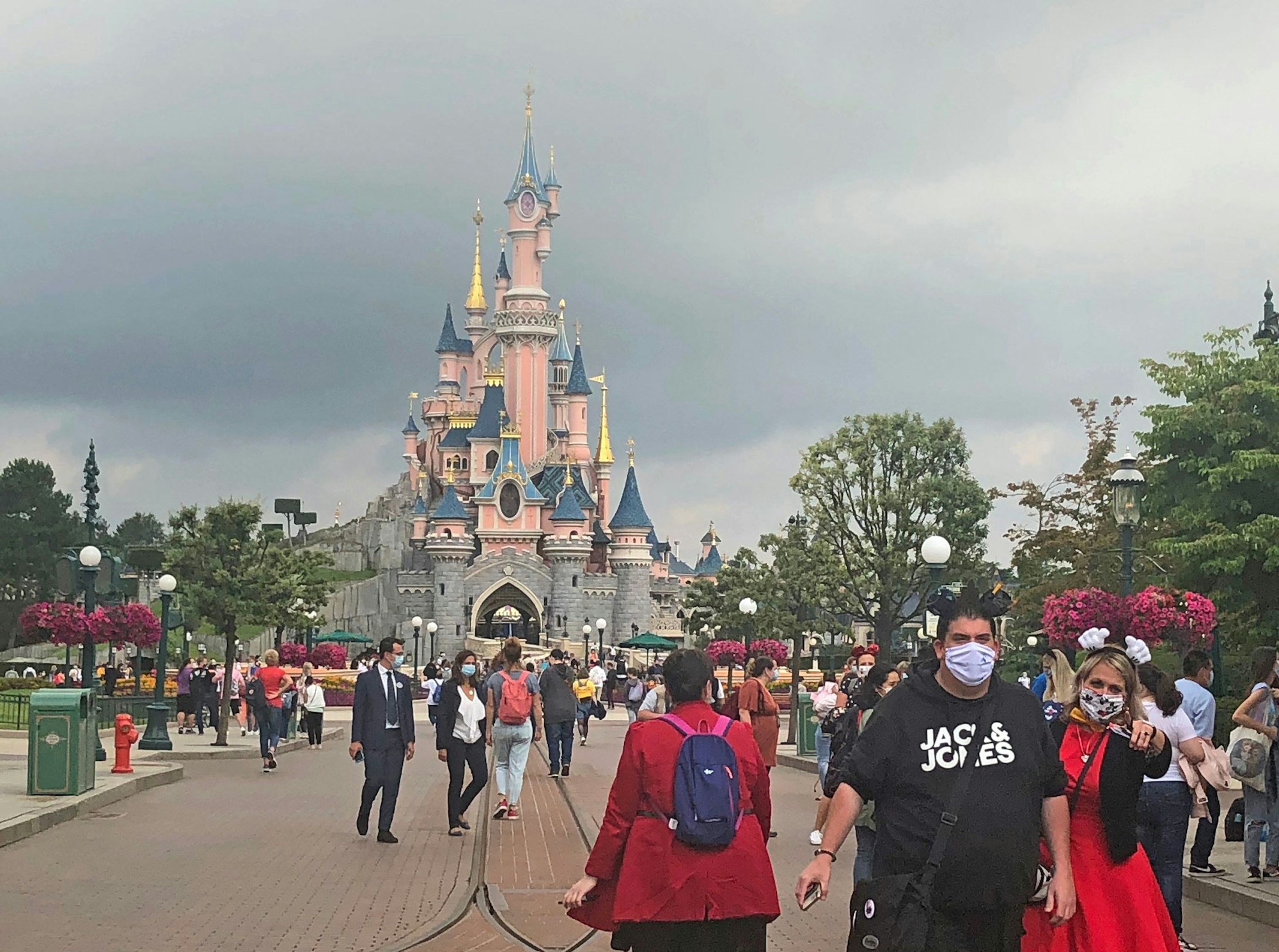Besucherinnen und Besucher spazieren über eine Straße vor dem Dornröschen-Schloss im Disneyland Paris.