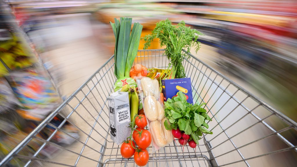 Ein mit Lebensmittel gefüllter Einkaufswagen wird durch einen Supermarkt geschoben.