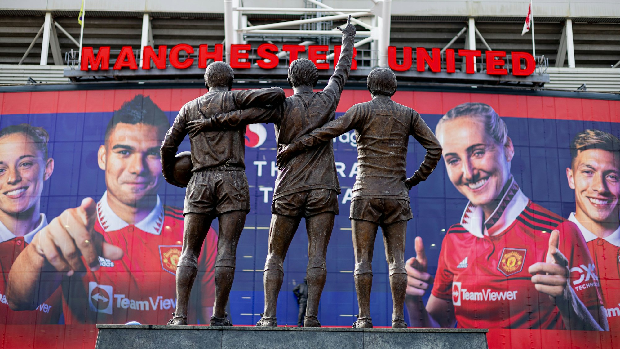 Ein Blick auf das Old Trafford und die Statue von George Best, Dennis Law und Bobby Charlton vor dem Stadion in Manchester.