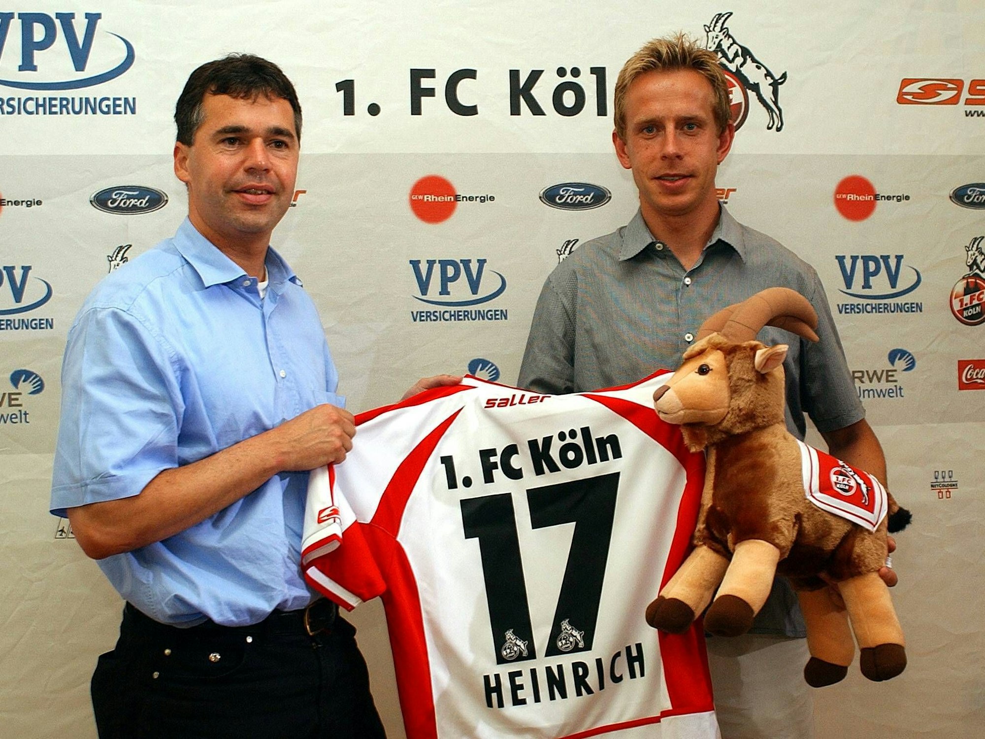 Andeas Rettig und Jörg Heinrich halten ein FC-Trikot mit der 17 hoch.