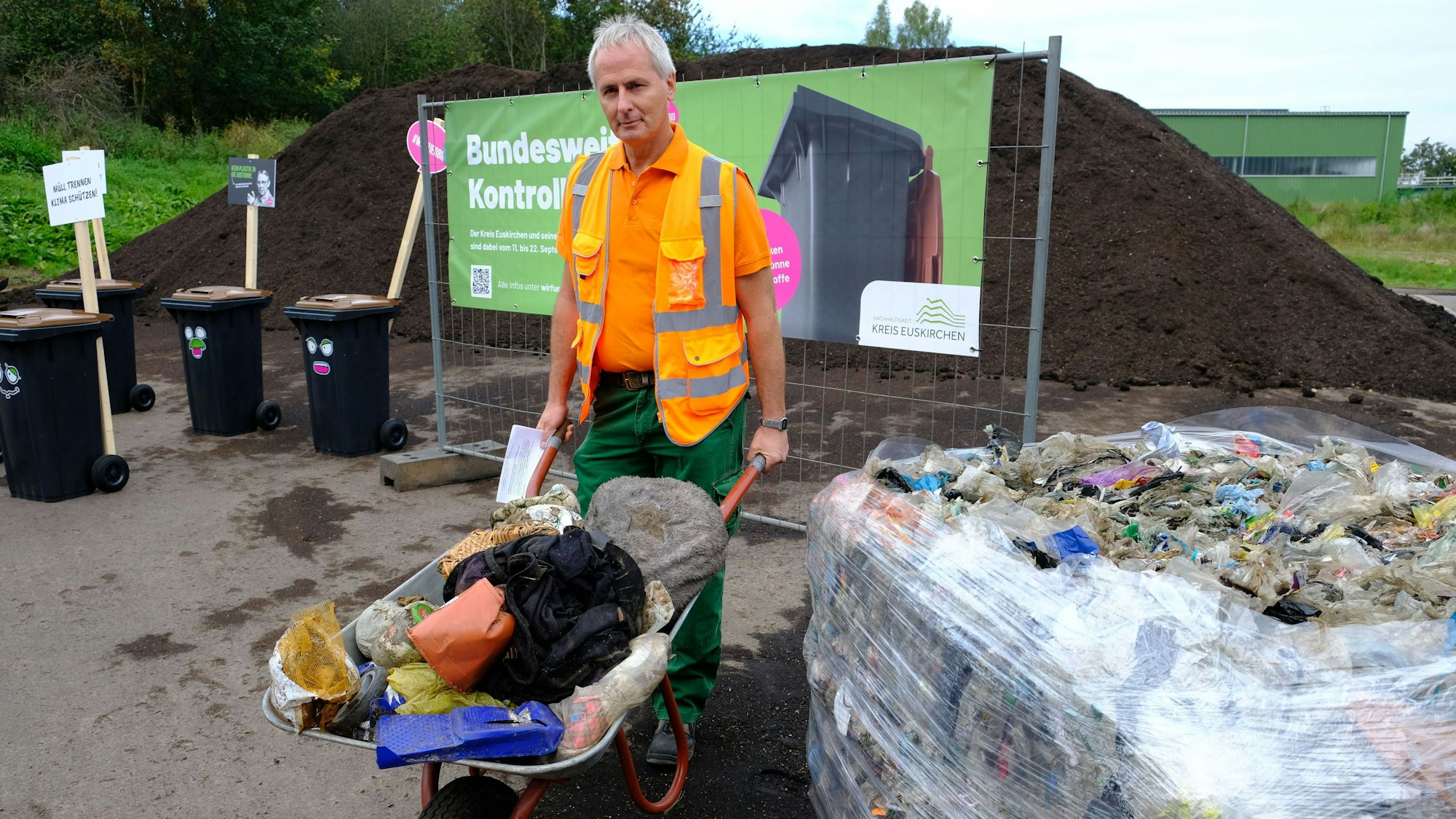 Norbert Lenzen mit einer Schubkarre voller Müll. Er trägt eine Arbeitsweste in Signal-Orange.