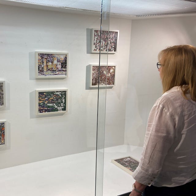 Eine Frau betrachtet kleinformatige Bilder, die an einer Wand hängen.