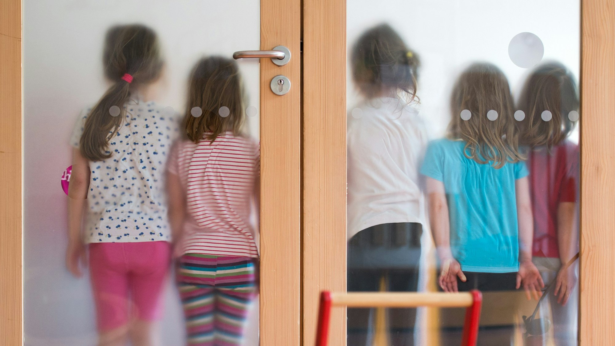 Kinder stehen mit dem Rücken an gegen eine Milchglastür gelehnt.