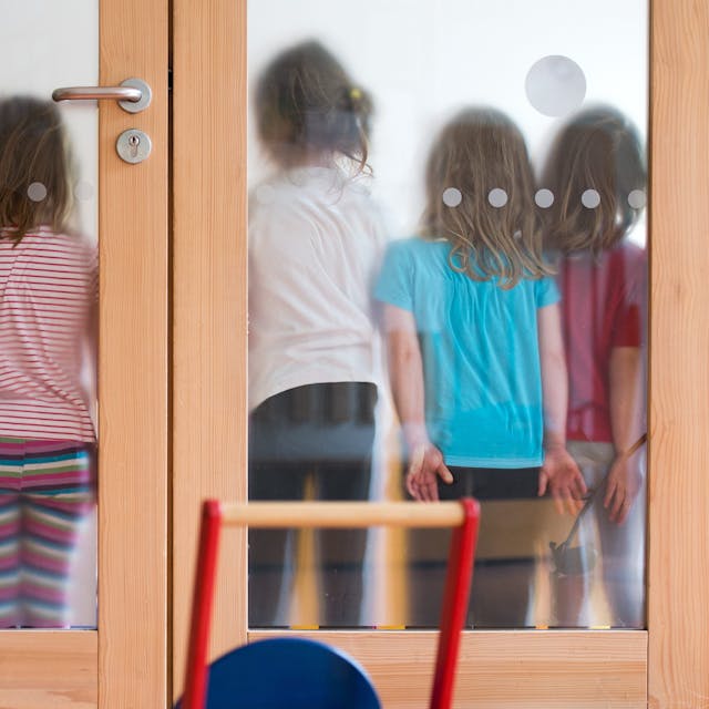 Kinder stehen mit dem Rücken an gegen eine Milchglastür gelehnt.