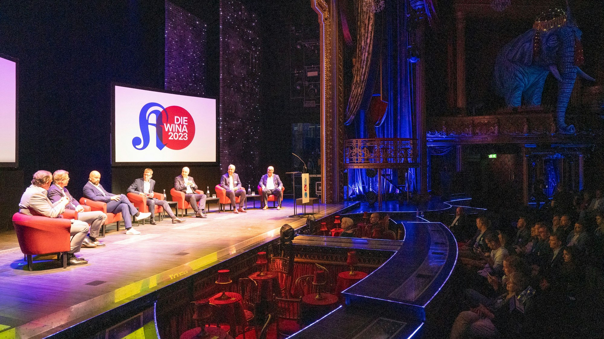 Wirtschaftsnacht Rheinland 2023: Die Panel-Diskussion zur Wirtschaft 2030 im Musical Dome. Im Hintergrund: Der Elefant des Musicals Moulin Rouge.