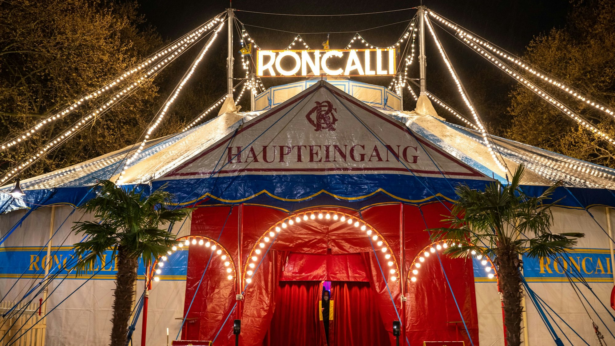 Das Roncalli-Zirkuszelt mit beleuchtetem Schriftzug am Abend ist zu sehen.