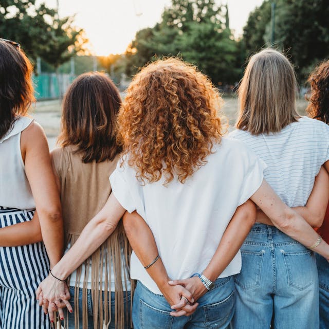 Eine Gruppe Freundinnen hält hinter dem Rücken Händchen.