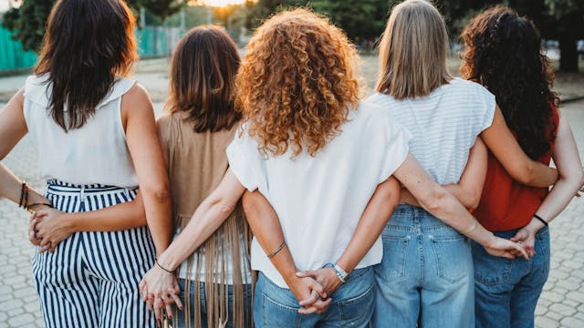 Eine Gruppe Freundinnen hält hinter dem Rücken Händchen.