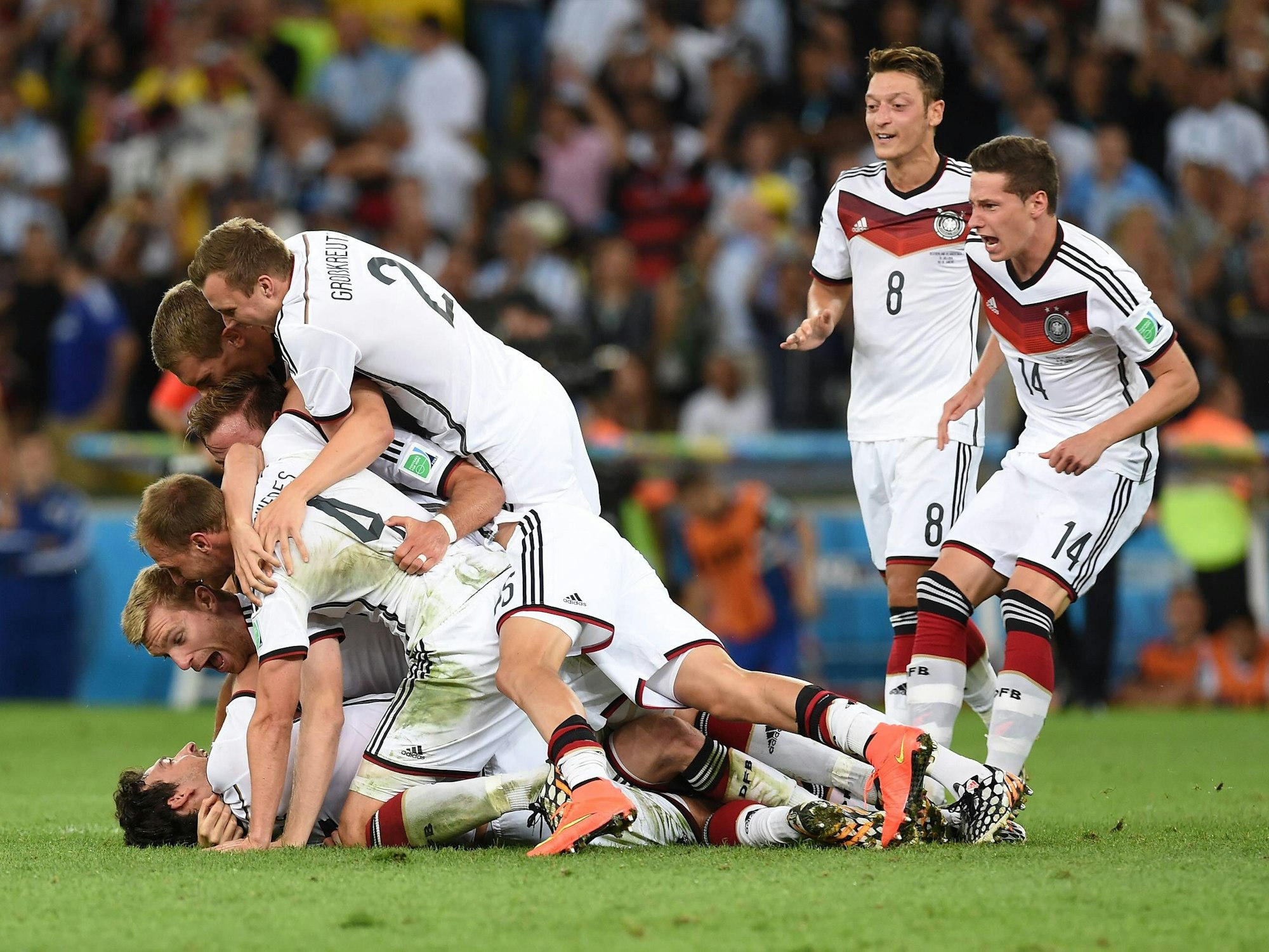 Die deutschen Nationalspieler liegen auf einem Haufen und jubeln. Mesut Özil und Julian Draxler sind dabei, sich zu ihren Kollegen zu werfen.