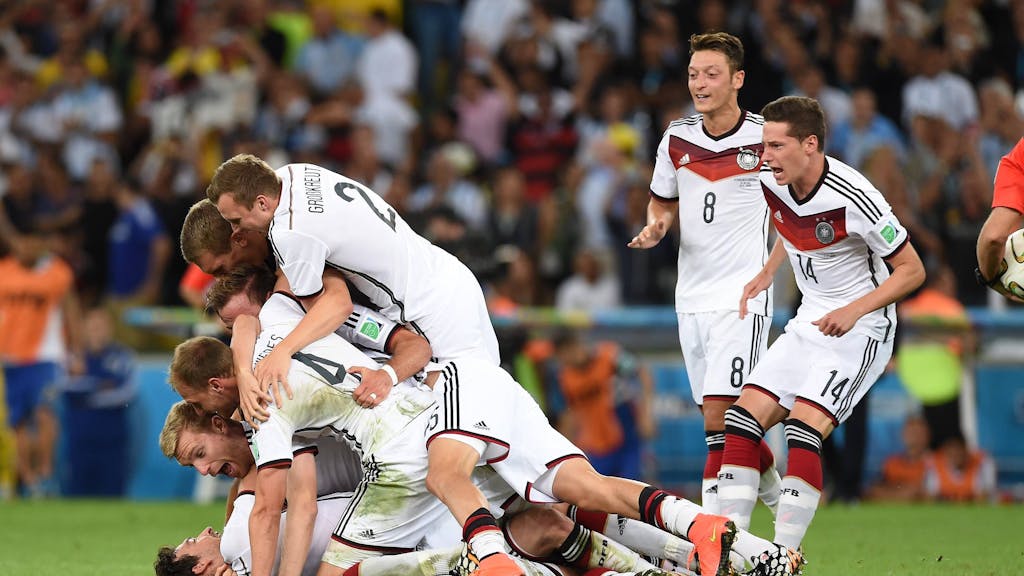 Die deutschen Nationalspieler liegen auf einem Haufen und jubeln. Mesut Özil und Julian Draxler sind dabei, sich zu ihren Kollegen zu werfen.