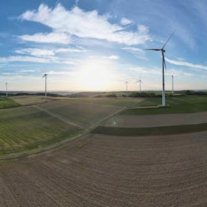 Windkraftanlagen stehen in einer Landschaft mit Feldern und Wäldern.