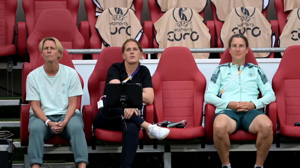 Bundestrainerin Martina Voss-Tecklenburg sitzt bei einem EM-Spiel neben ihrer Co-Trainerin Britta Carlson und Teampsychologin Birgit Prinz.