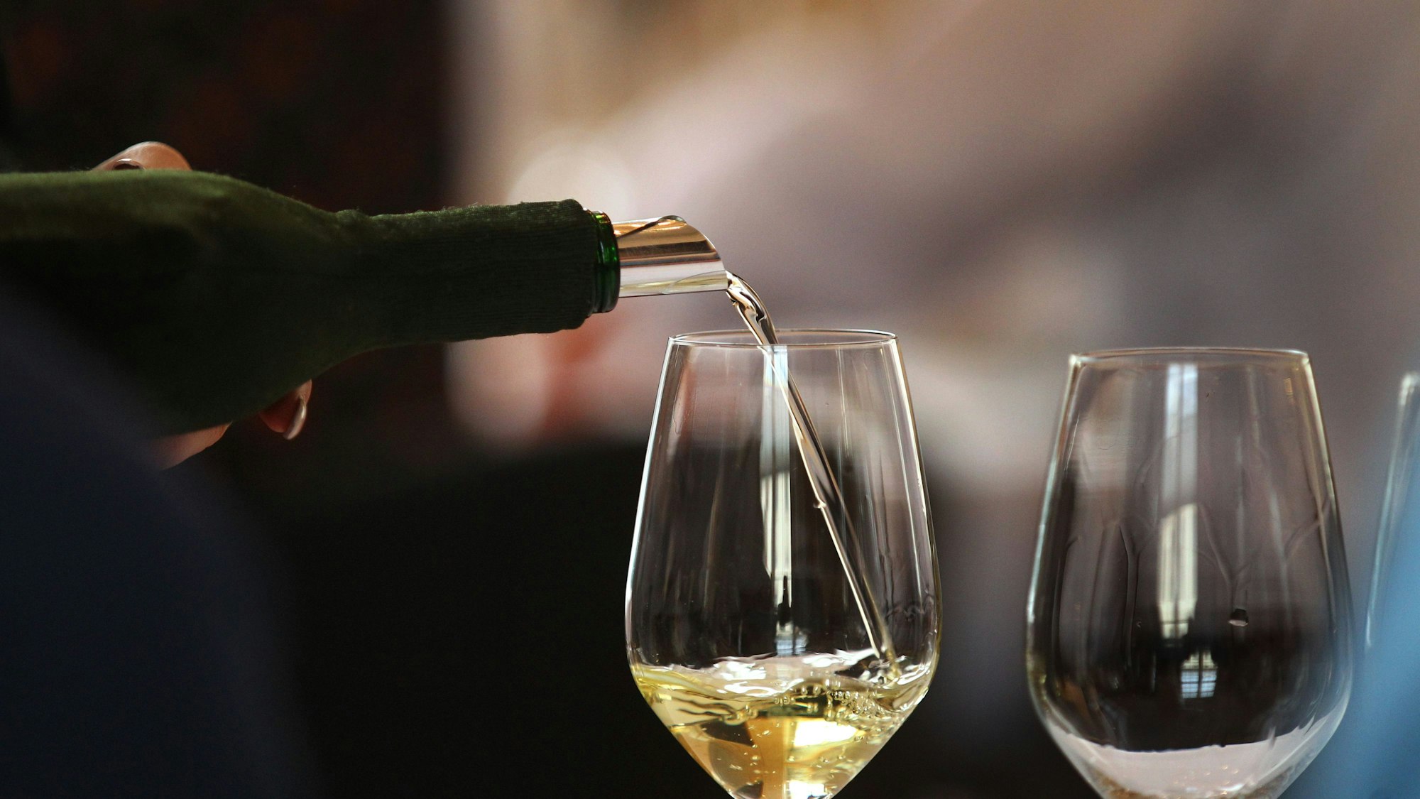 Aus einem verdeckten Bocksbeutel wird bei einem Wein-Wettbewerb ein Glas mit Weißwein gefüllt.