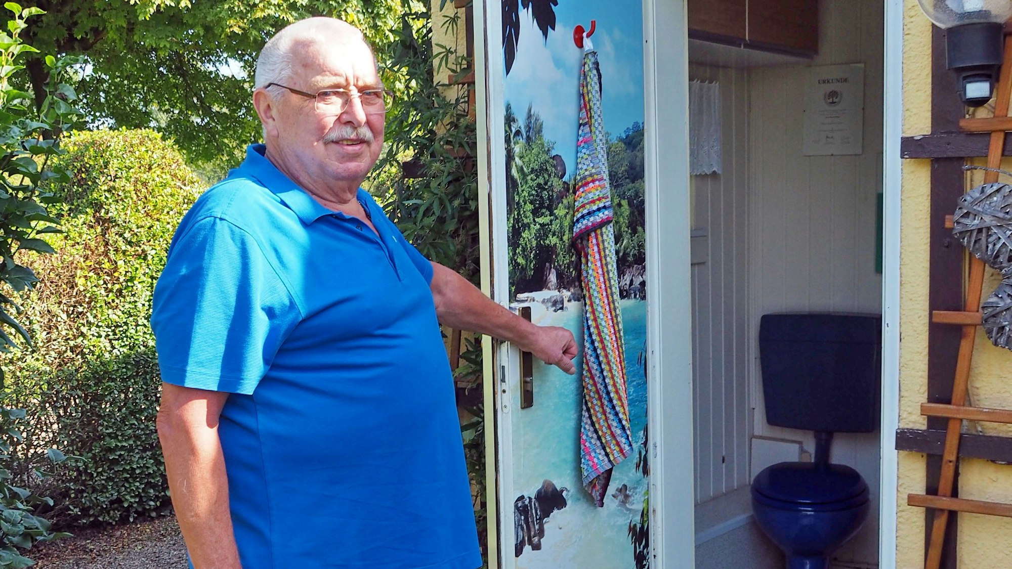 Ein älterer Mann hält die Tür zu einem Toilettenraum auf.